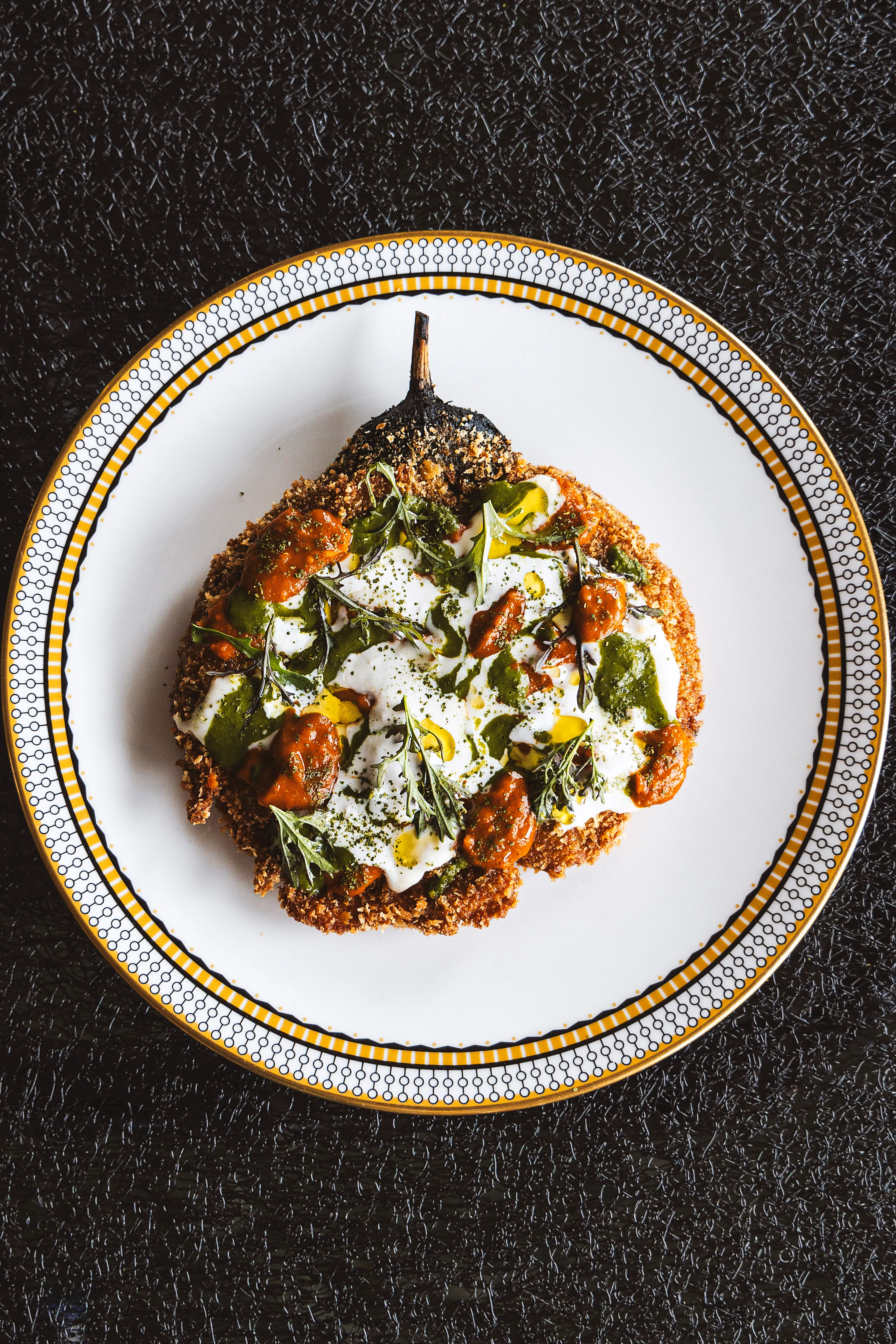 Breaded aubergine with yogurt, tomato and herbs on a gold-rimmed plate