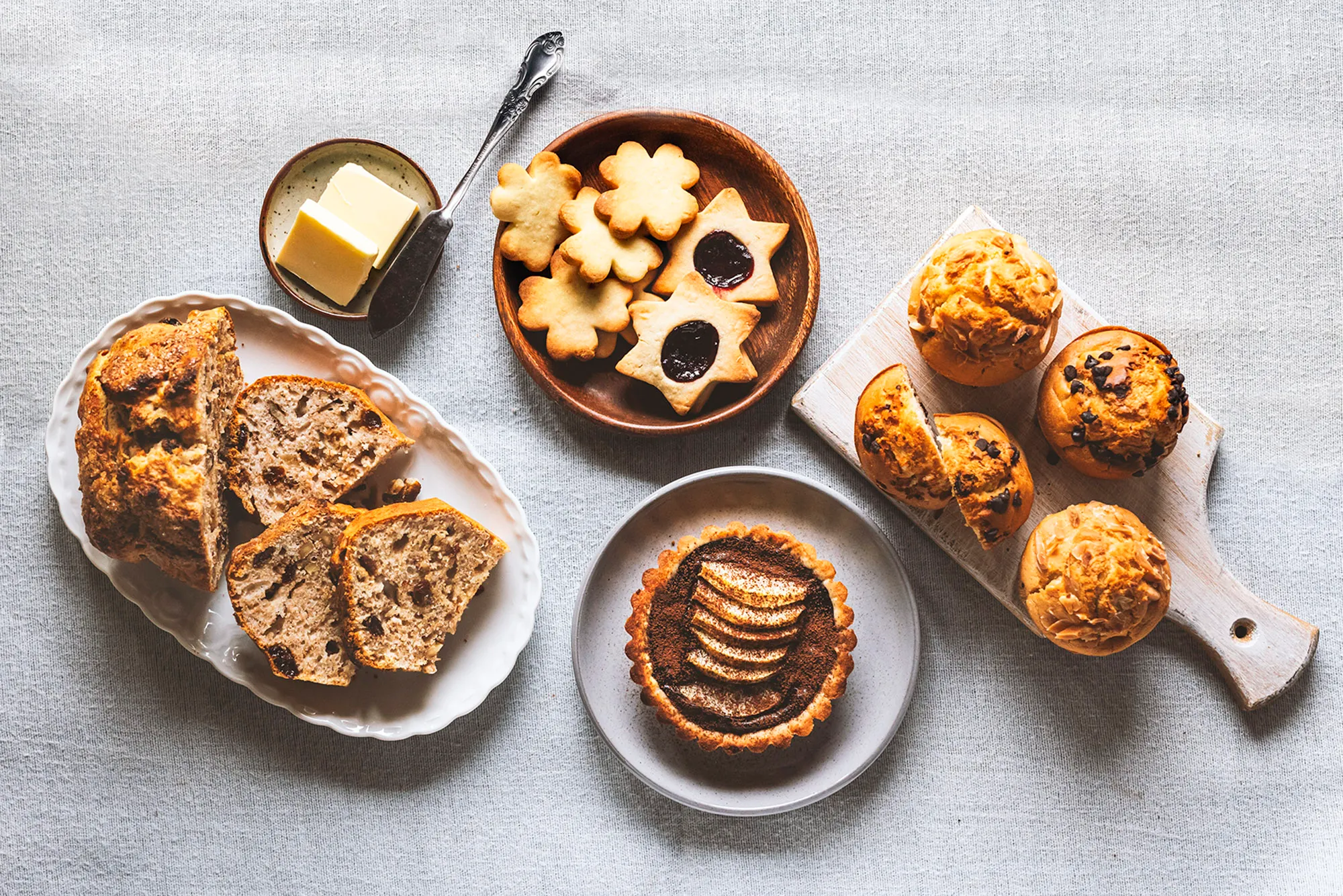 Sliced bread, biscuits, muffins and a tart with butter