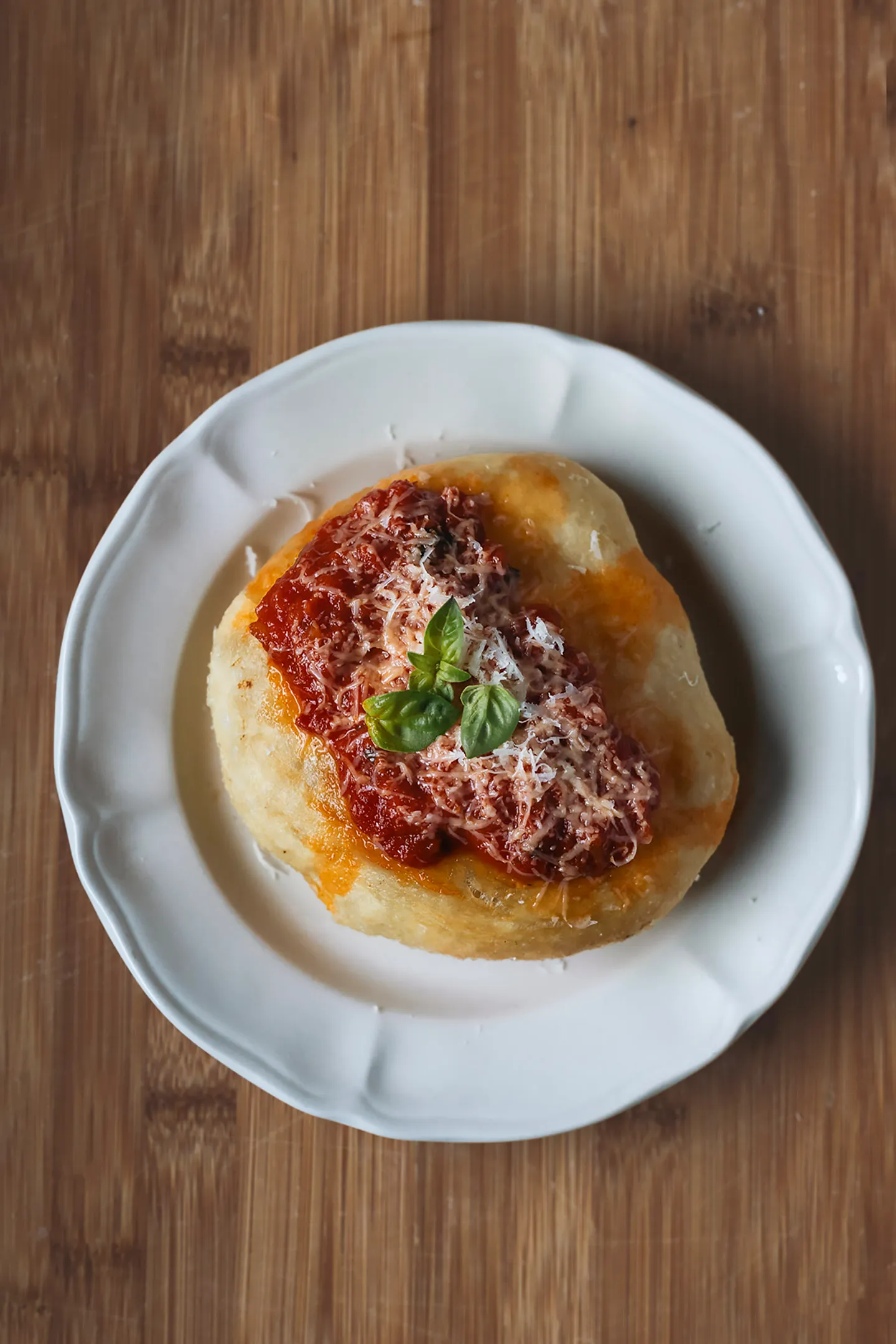 Fried pizza with tomato, parmesan and basil on a white plate