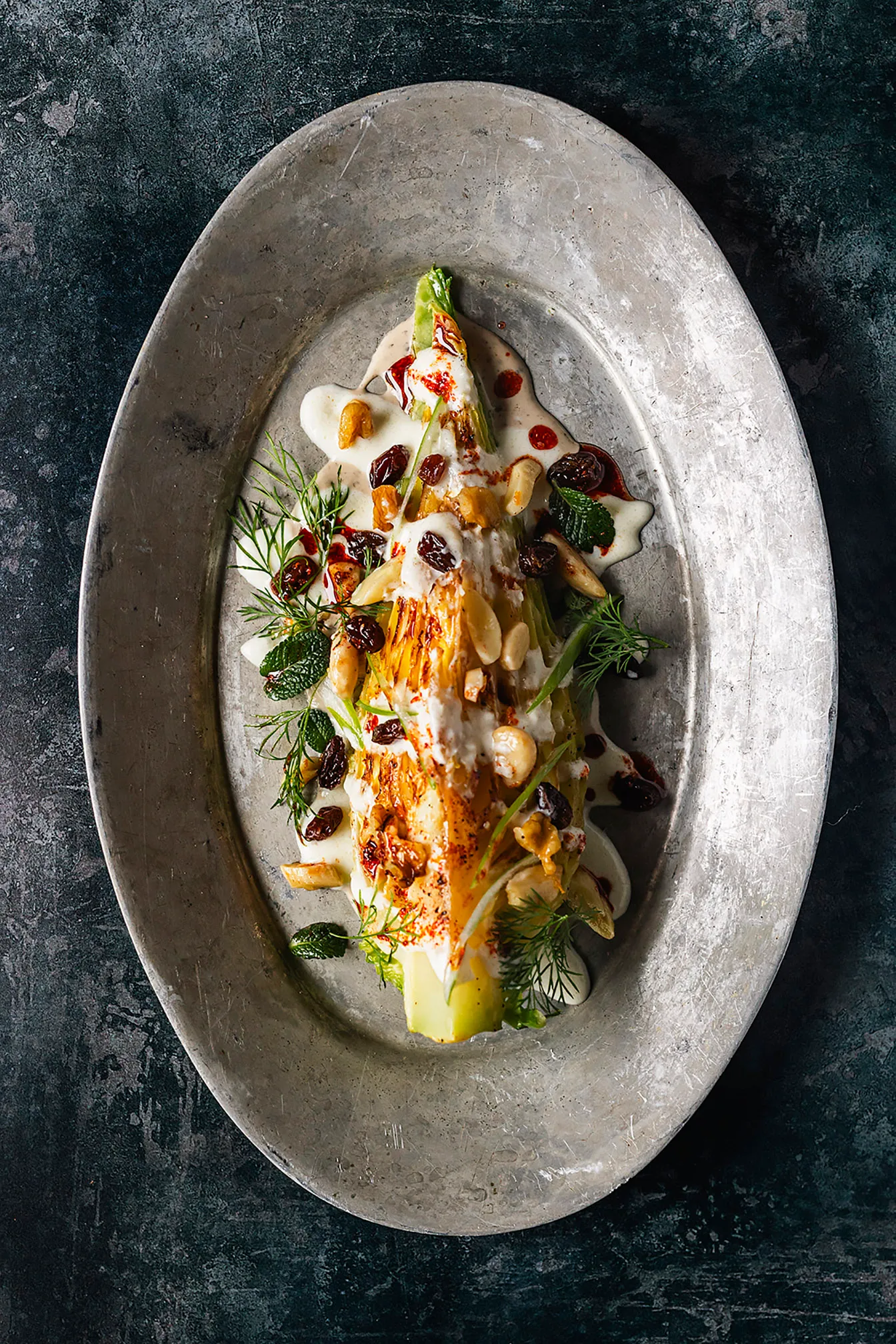 Grilled lettuce heart with cream, nuts and raisins on a pewter platter