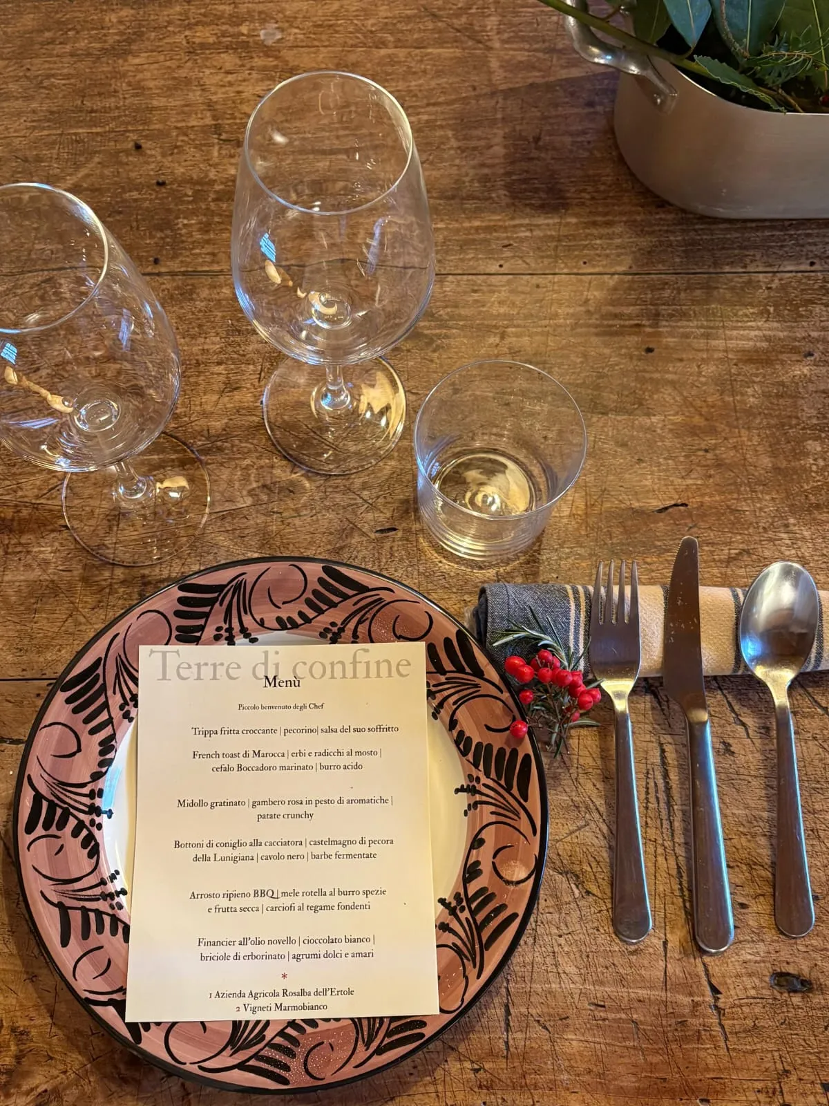 Printed dinner menu on a plate beside cutlery and wine glasses